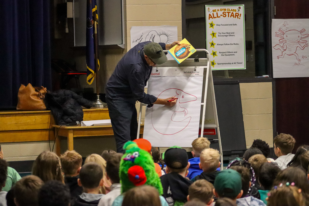 Students watch illustrator create drawing on large chart paper