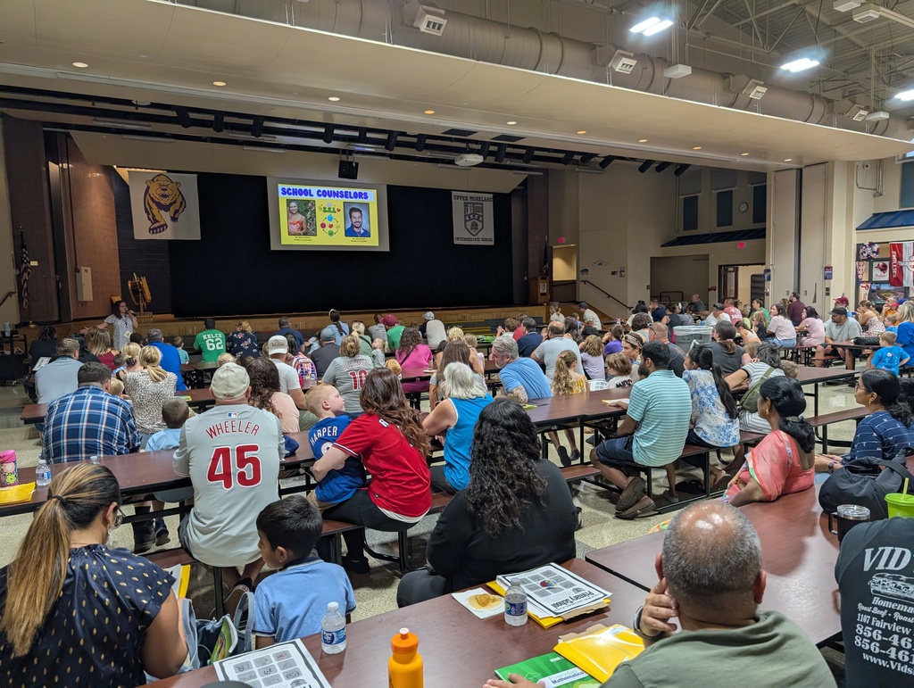 Group of UMPS families sitting in the Cafetorium and listening to a presentation from the principal