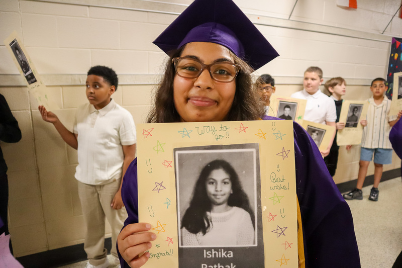 Senior student in graduation attire holds a sign with a picture of herself from Intermediate School
