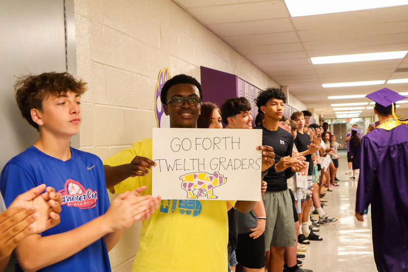 Student in the Middle School holds a sign reading 'Go Forth Twelth Graders' with a bear drawing in the Middle School hallway
