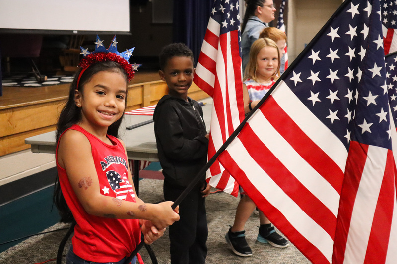 Students pose smiling holding American Flags