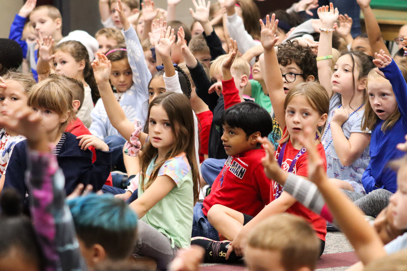 Group of students in assembly are raising their hands