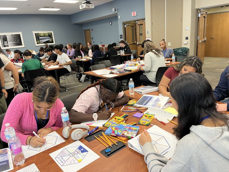 Students using art supplies to color worksheets at tables.