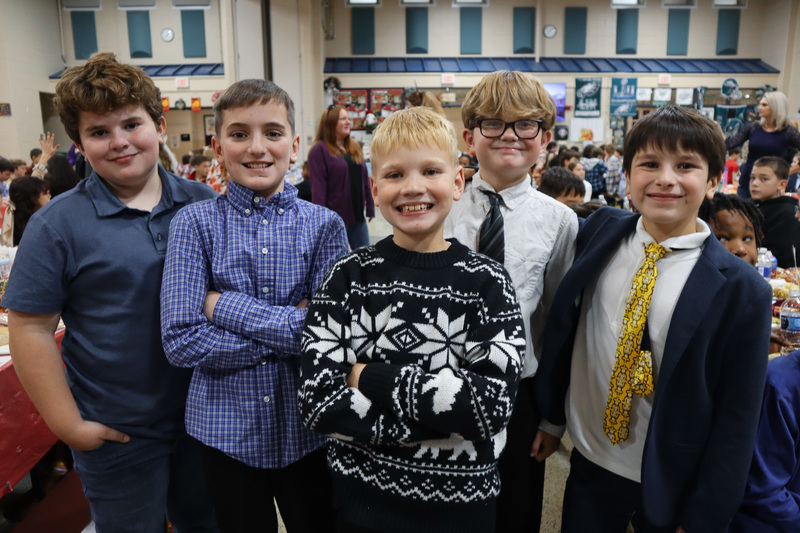 Five boys smiling and standing together in a large indoor venue.