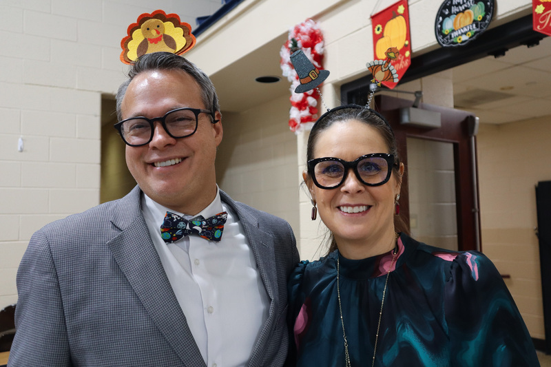 Two people smiling, wearing glasses and festive Thanksgiving-themed headbands.