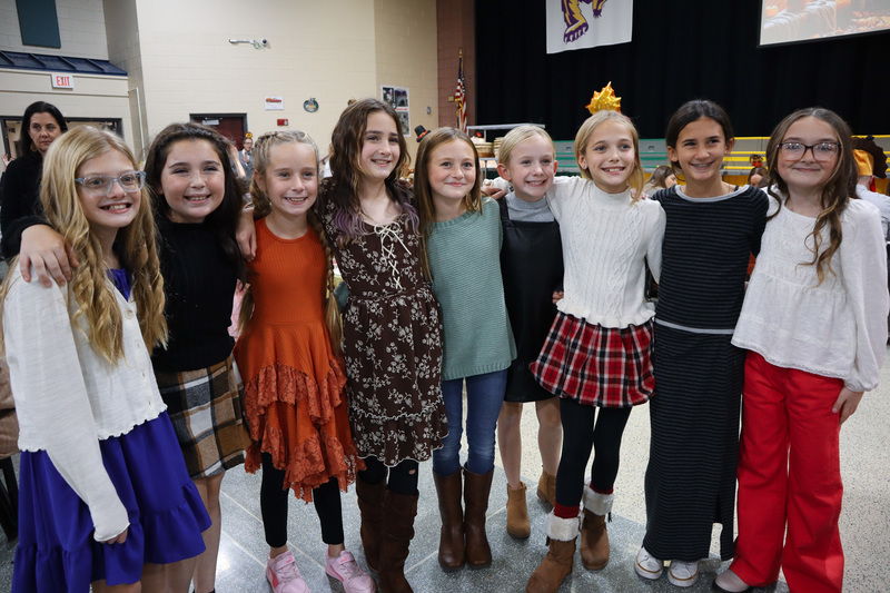 Group of nine young girls standing together, smiling, dressed in colorful outfits.