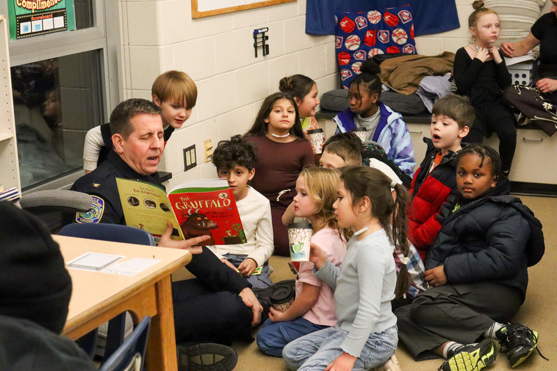 * A group of students sit on the floor with a member of our Police Department as he reads a book to them