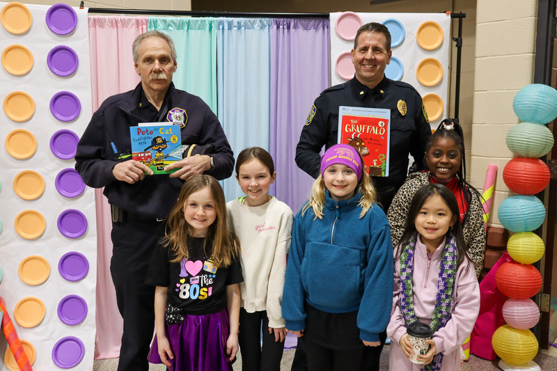 * Group of five students stand in front of a colorful backdrop alongside members from our Police and Fire Departments