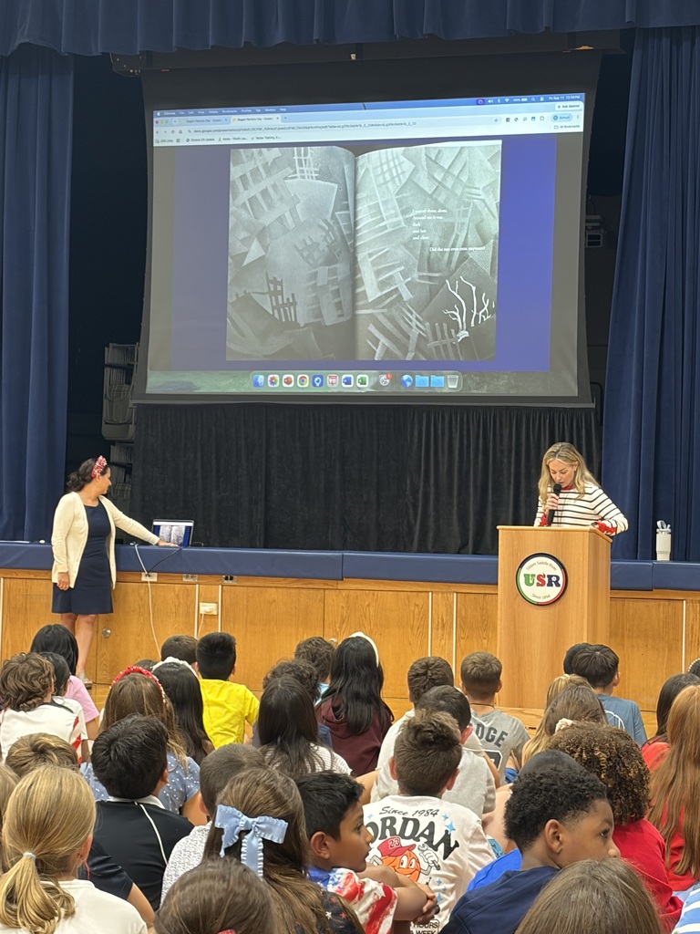 A teacher reads a book at a school assembly.