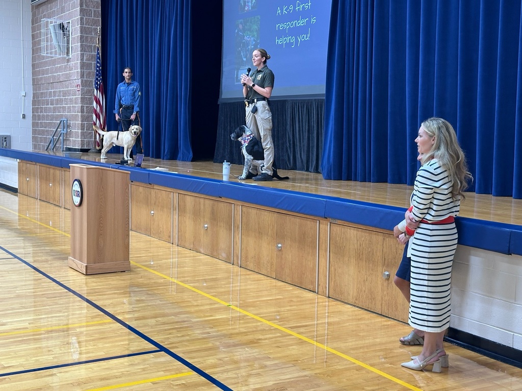 Two police stand on a stage speaking to an audience with K9 dogs at their sides. 