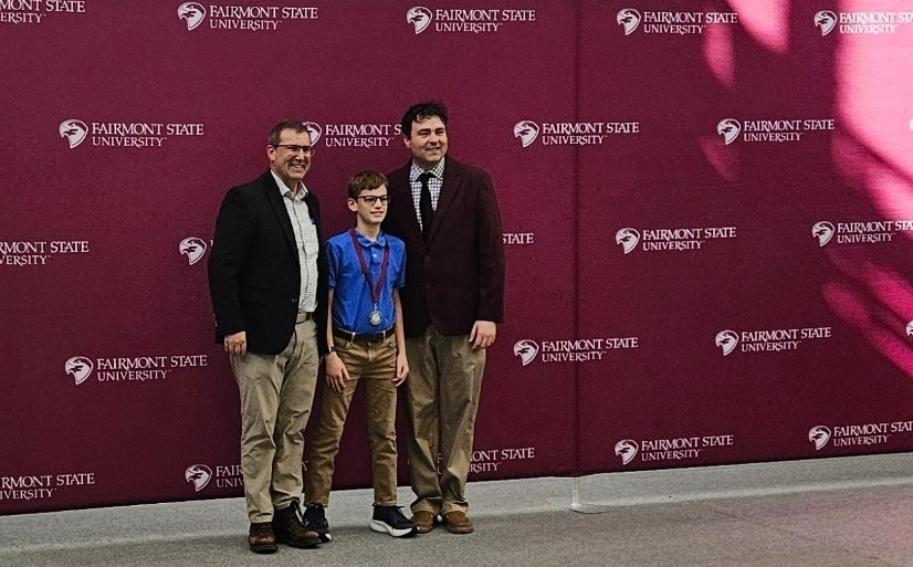 3 males standing infront of the Fairmont College Logo
