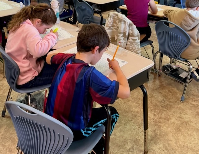 Students working in a classroom with pencil and paper at their desks.