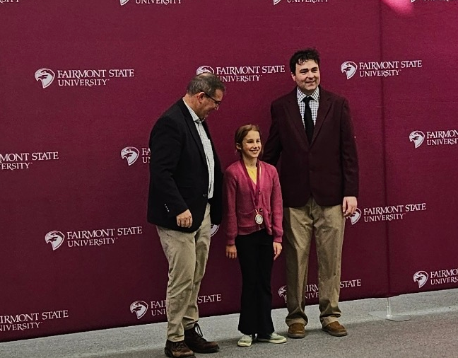 Image of 2 males and a female standing infront of the Fairmont State University Logo