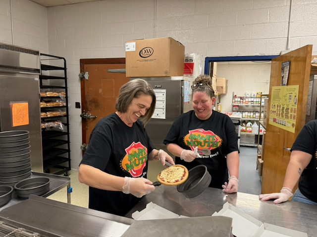 Cooks preparing smart mouth pizza, smiling.