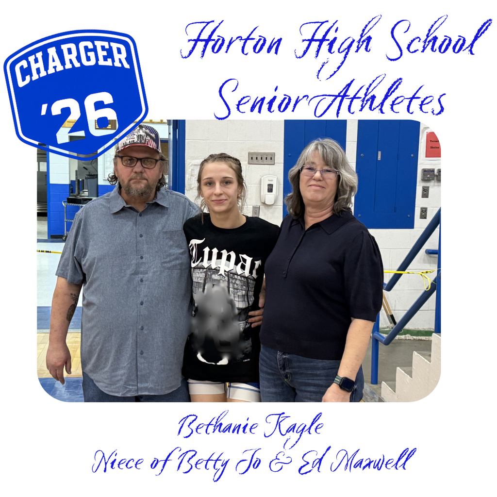 Three people pose in a school gym. One wears a gray shirt, one a black shirt, and the third a cap.