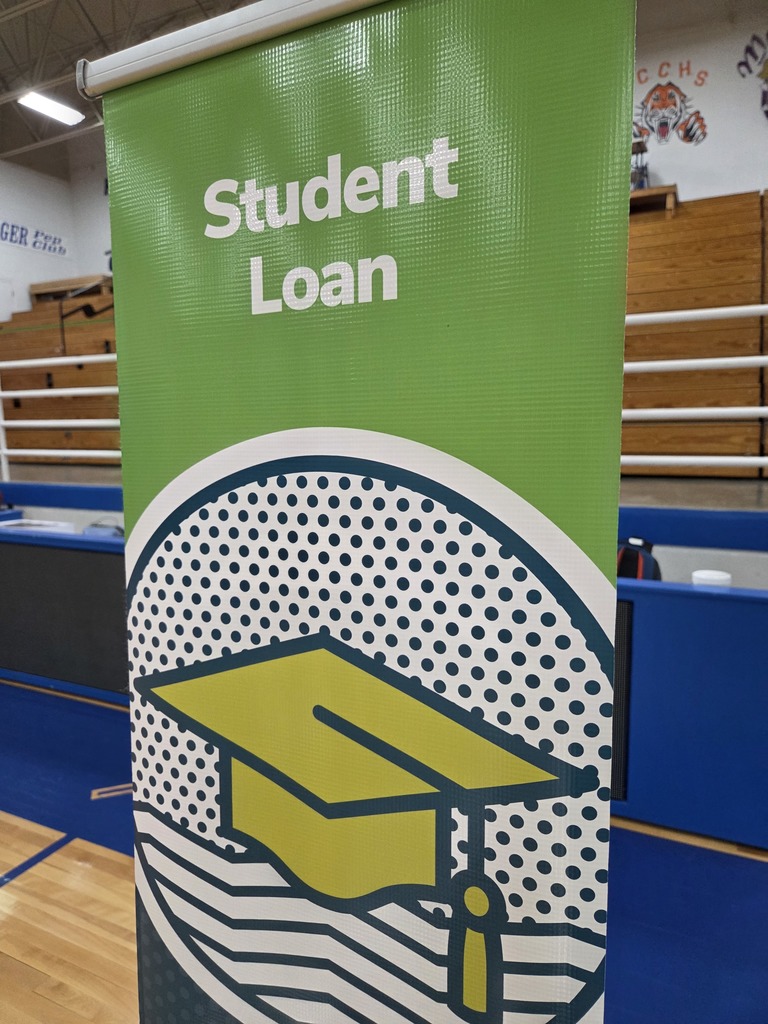 A green banner with a graduation cap design displays "Student Loan" in a gymnasium. Blue benches and a wooden railing are in the background.