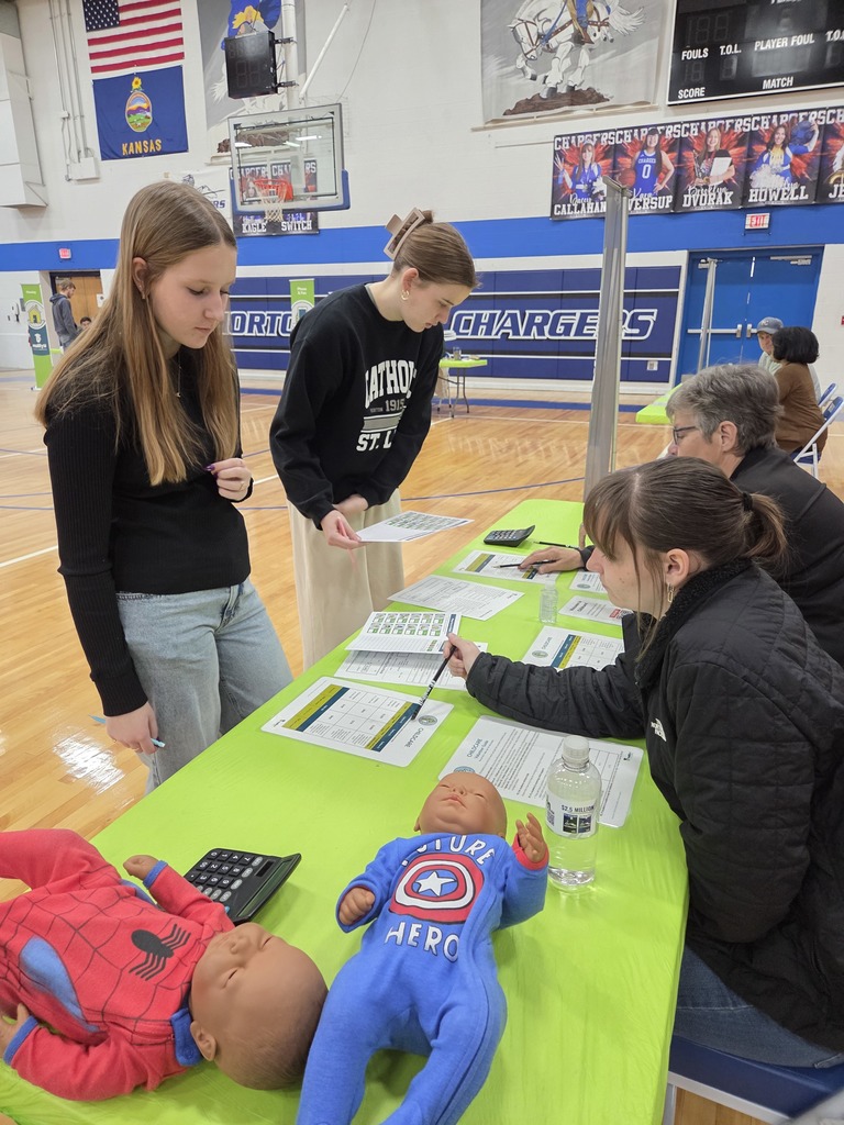 Four people at a table with a table cloth. One person is writing on a paper.