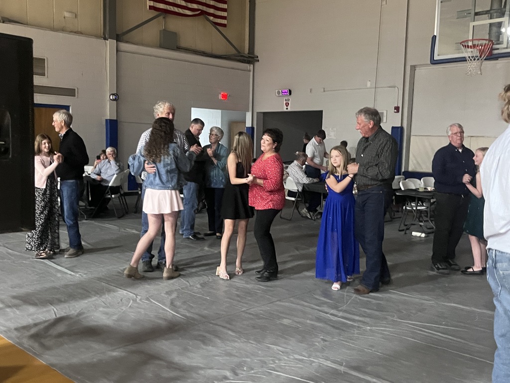 A group of people dancing in a gymnasium with a basketball court visible in the background.