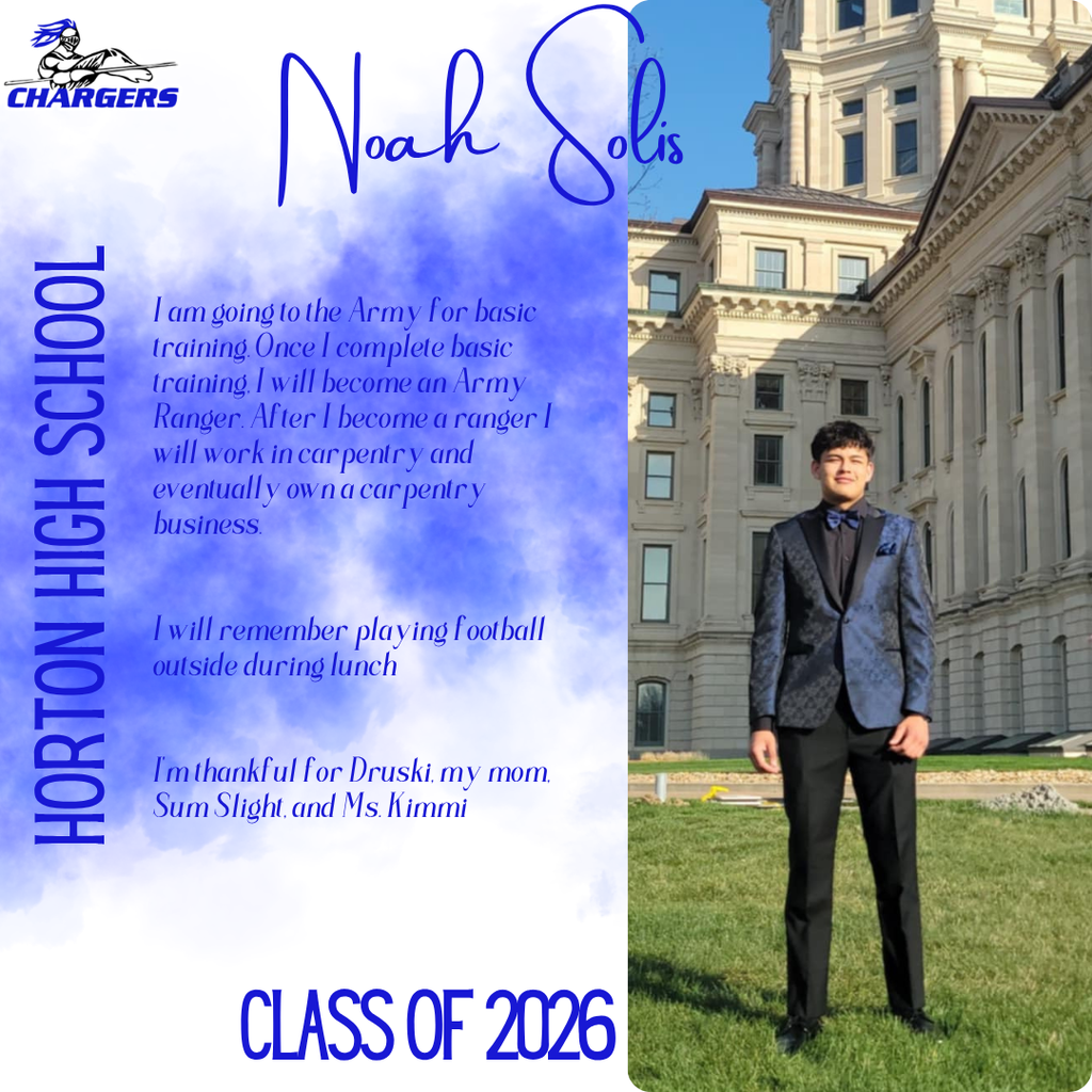 A man stands on a lawn in front of a building. He wears a suit and a bowtie.