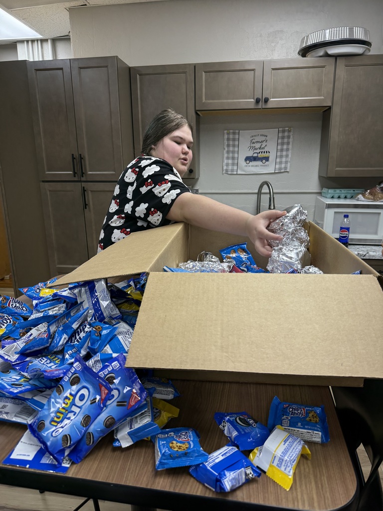 Person standing by a table with a box of packaged snacks. The box is open and full of food.