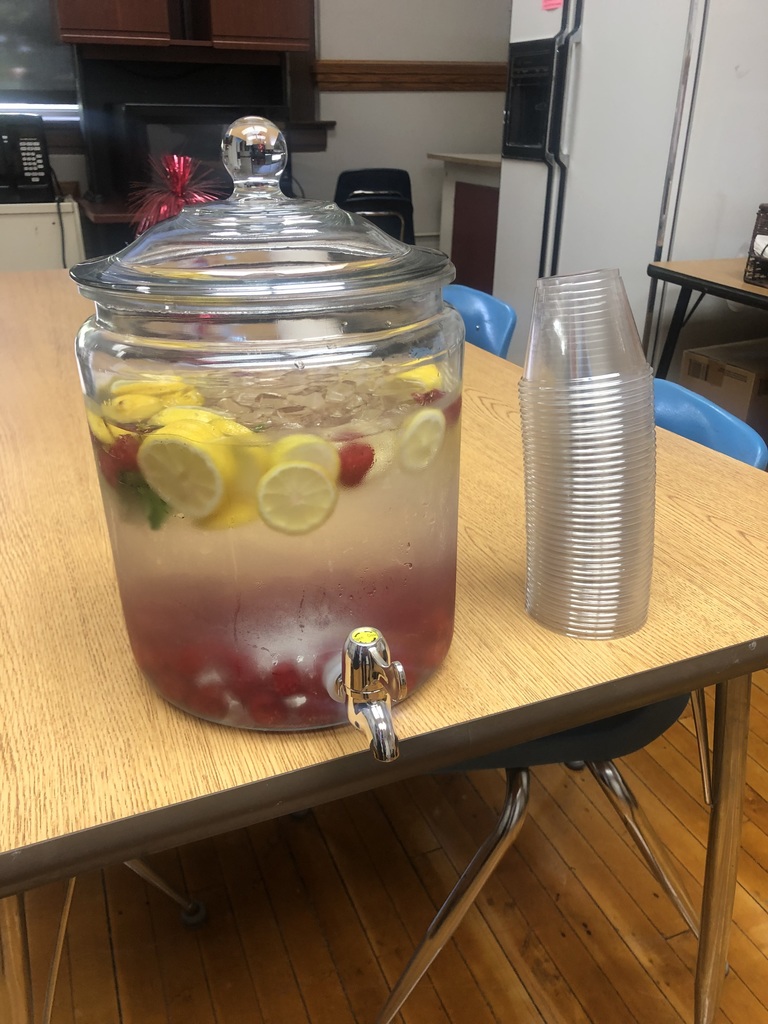 A pitcher with a spout contains a drink with berries, lemons, and water on a wooden table.