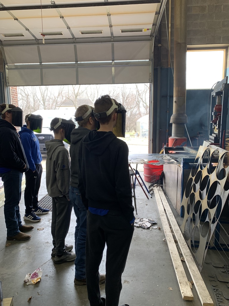 Six people wearing goggles in a garage with a metal structure and a large window.