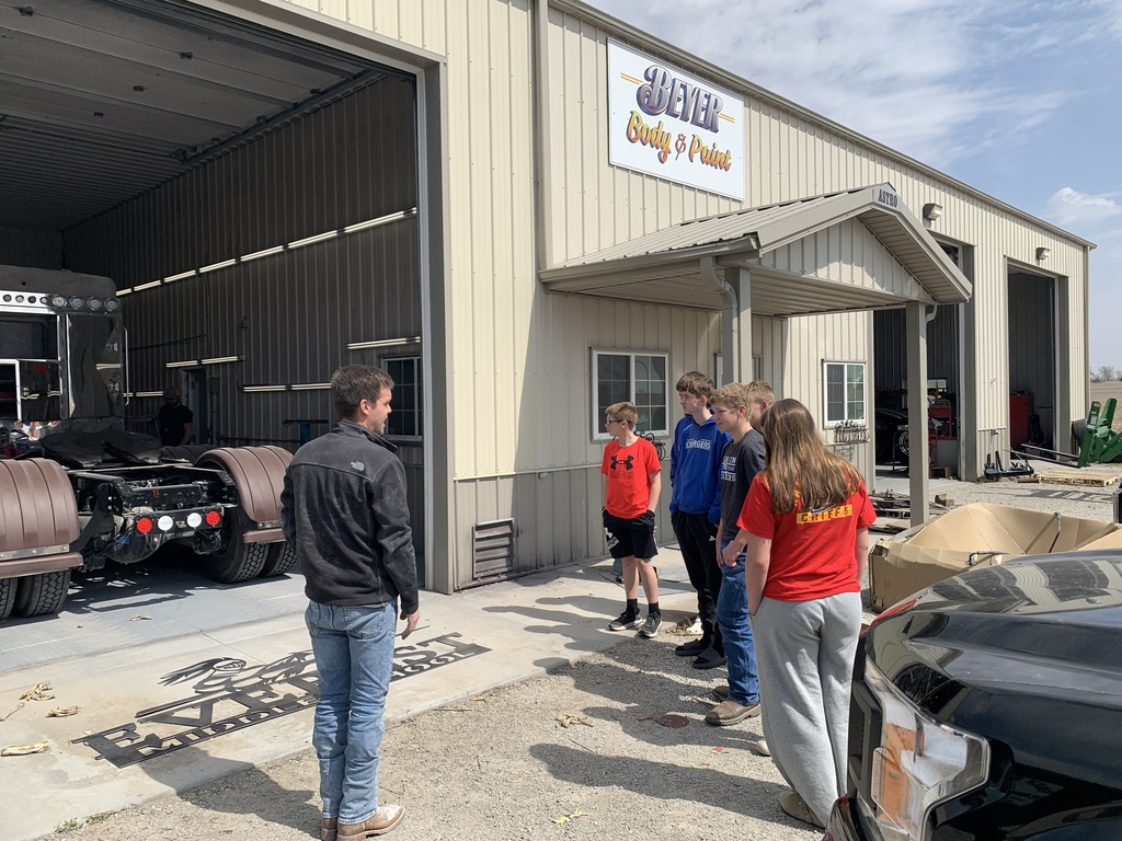 A group of people stands in front of a large building labeled "Steel." Vehicles are parked nearby.