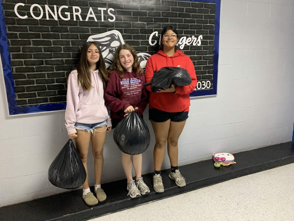 Three girls hold bags in front of a brick wall with "CONGRATS" and "O30" written on it.