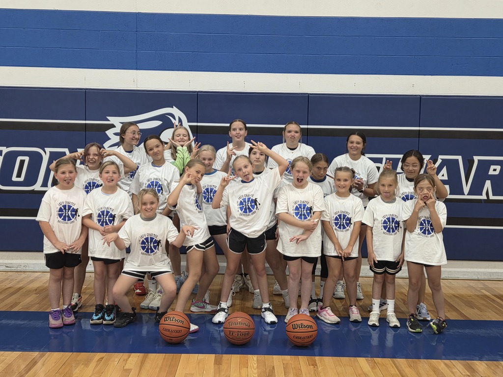 A group of girls in white T-shirts and shorts on a basketball court, posing for a team photo.