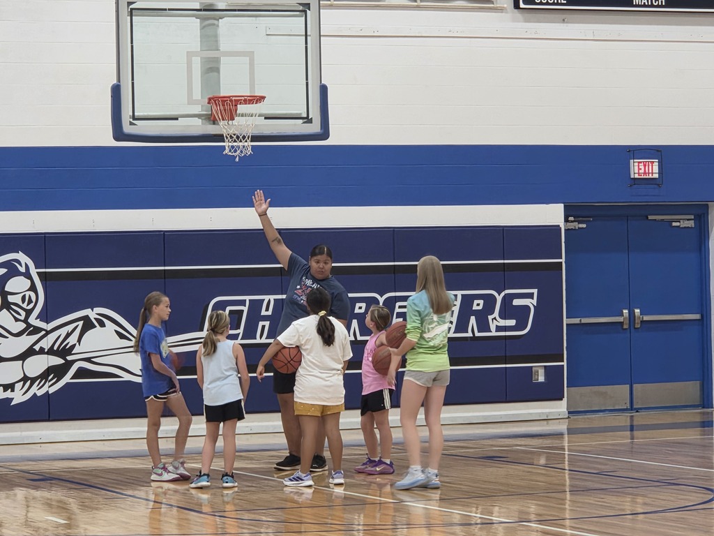 Five young girls and a man with a hat are standing in a basketball court. The walls are blue with white trim.