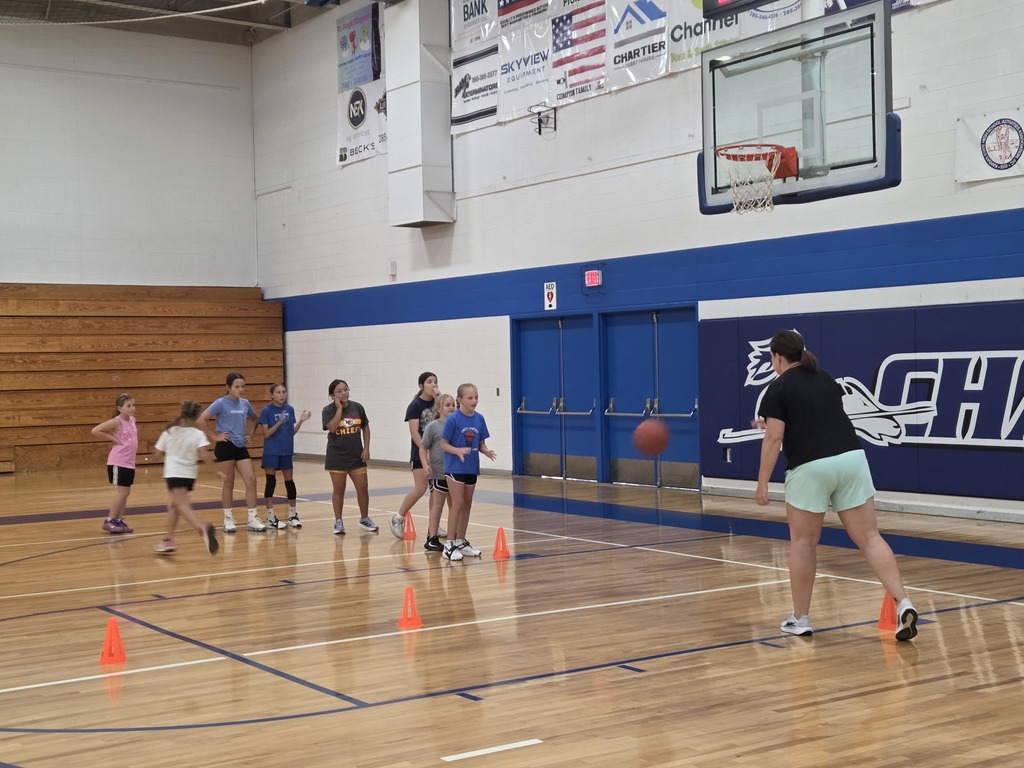 An indoor basketball court with a group of people practicing basketball. Orange cones mark the playing area.