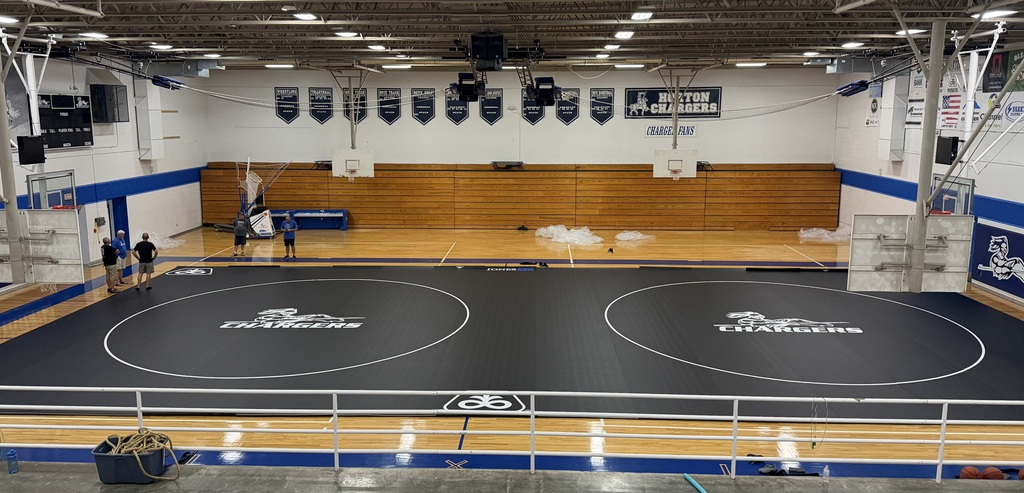 An indoor gym with two wrestling rings and a wooden floor, surrounded by a white railing.
