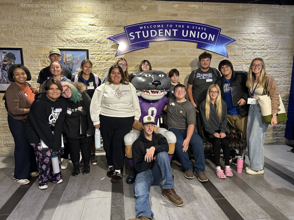 Group of people in casual clothing posing for a picture with a mascot in a room.