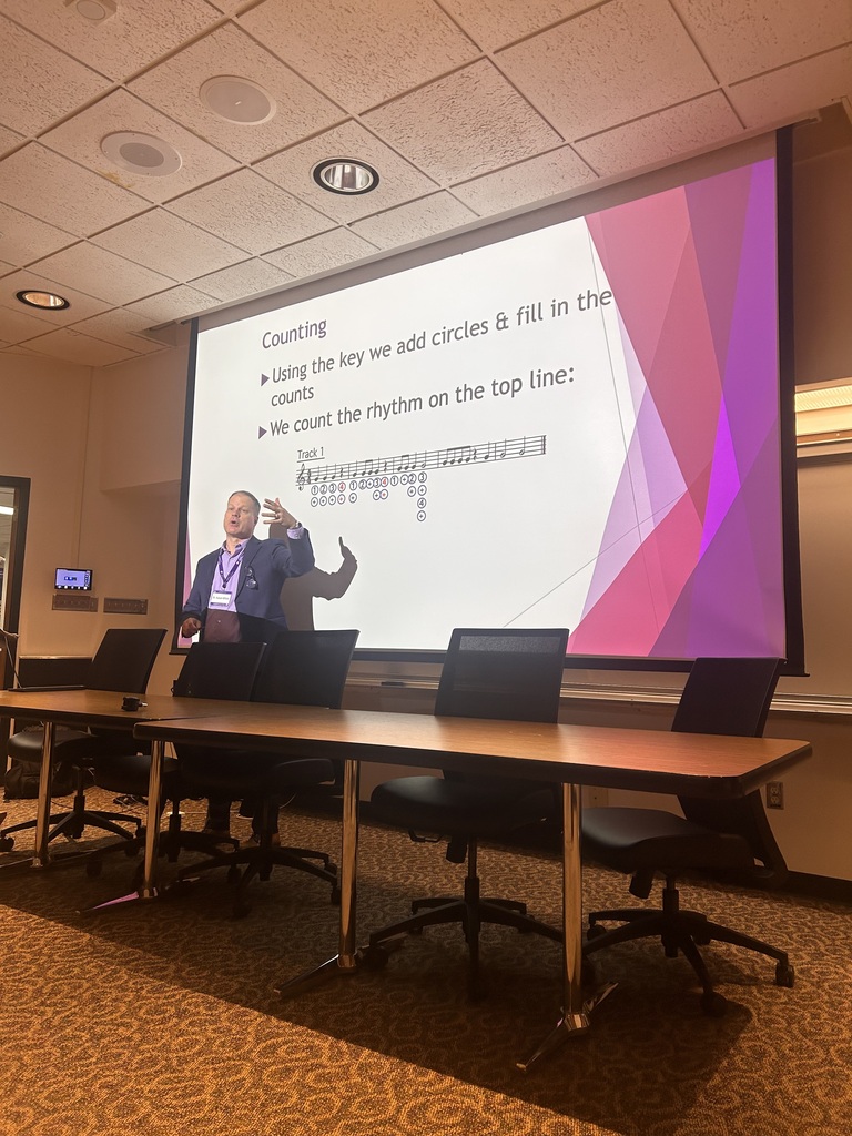 Meeting room with a person standing before a projector screen with a presentation on it.