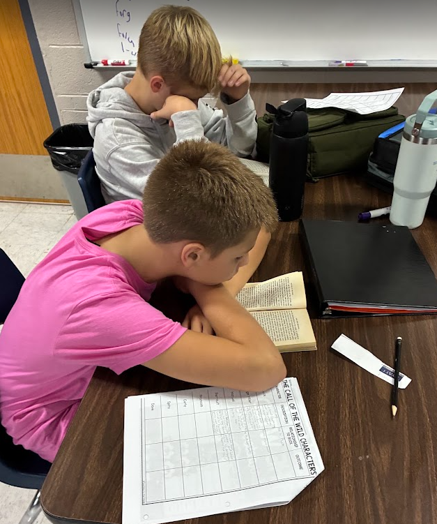 Two boys sit at a desk reading a book