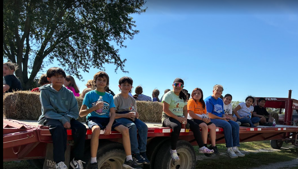 A group of children sitting on a flatbed trailer filled with hay bales on a sunny day.