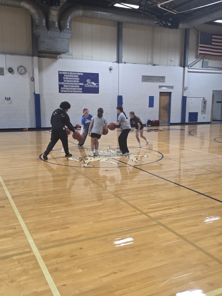 A group of people playing basketball on an indoor court, wearing sports gear, in an indoor sports facility.
