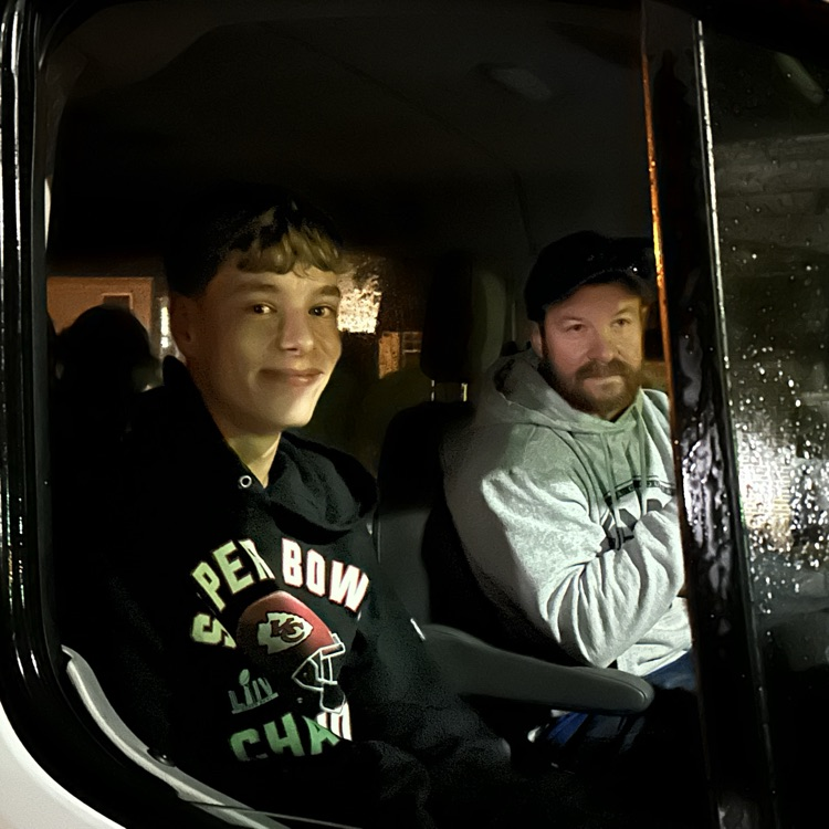 Two people inside a vehicle with a white frame; one smiling while looking at the camera.
