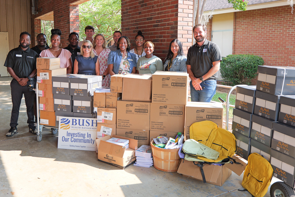 Group photo of donors and VCS staff behind donated items like boxes, supplies, and book bags