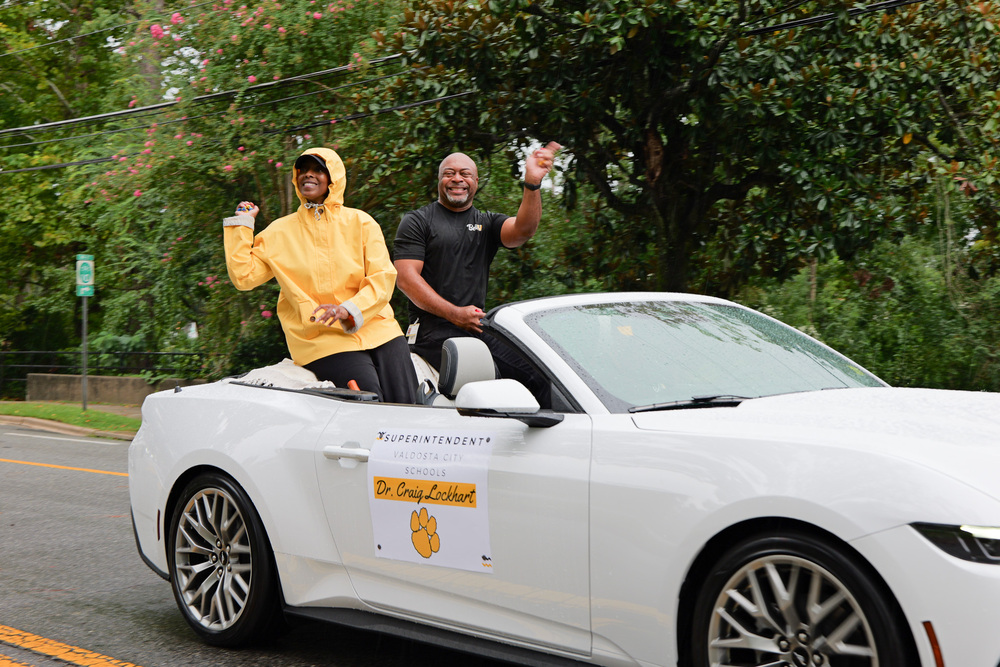 Dr. C Lockhart & Dr. T Lockhart waving, smiling, and throwing candy from a car