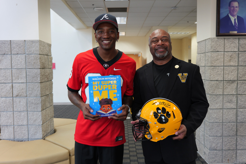 Malcolm holding his book with Superintendent Dr. Lockhart holding a wildcat football helmet