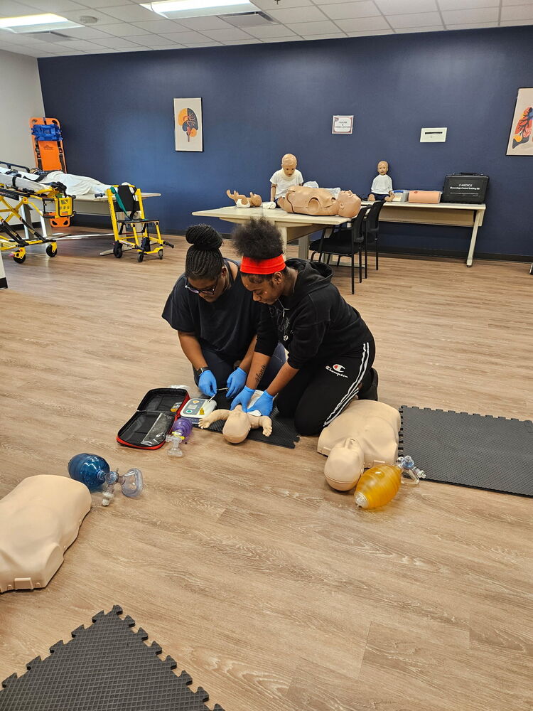 two students practicing CPR on a baby prop