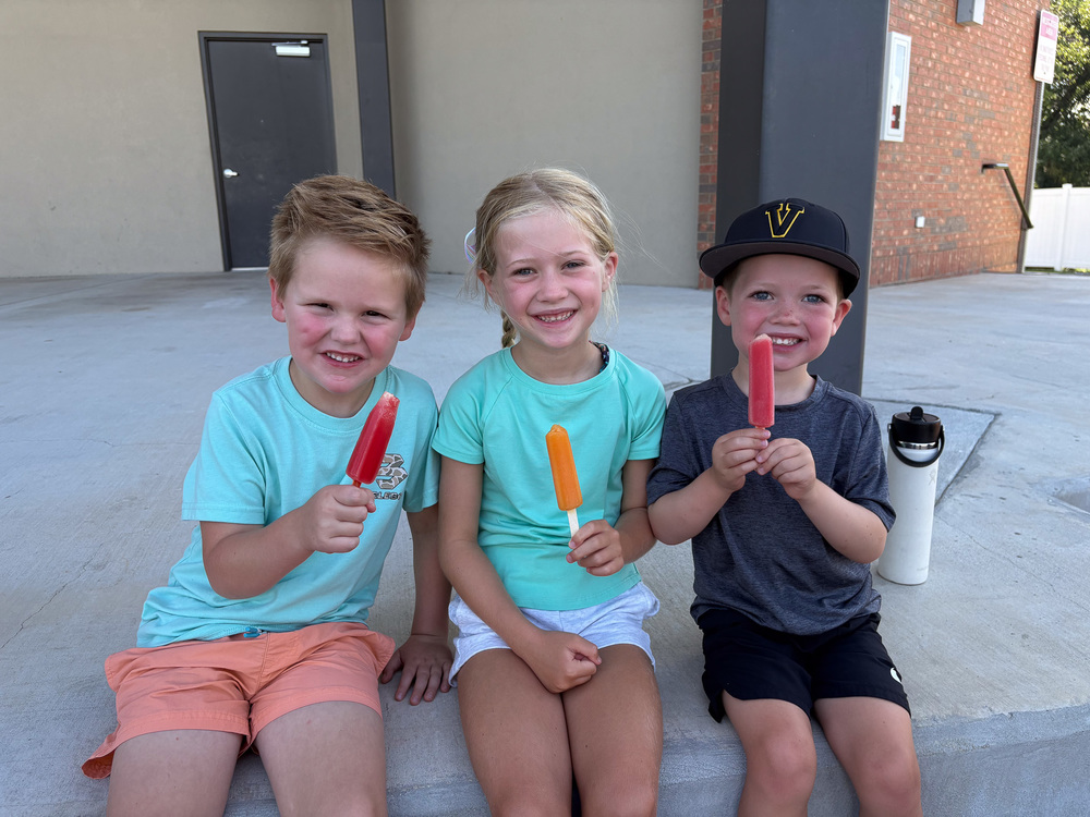 Three kids holding popsicles and smiling at the literacy event