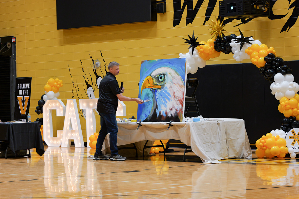 Mr. Glenn, painting an eagle in front of black and gold balloon arch and CATS light up letters