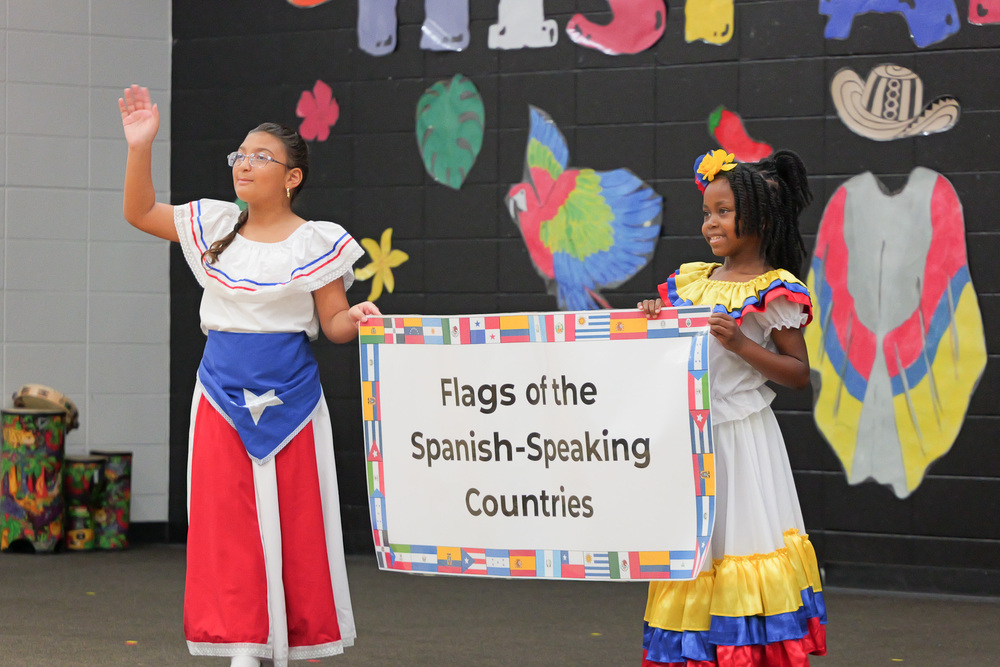 two students in heritage themed outfits holding a sign that says Flags of the Spanish-Speaking Countries