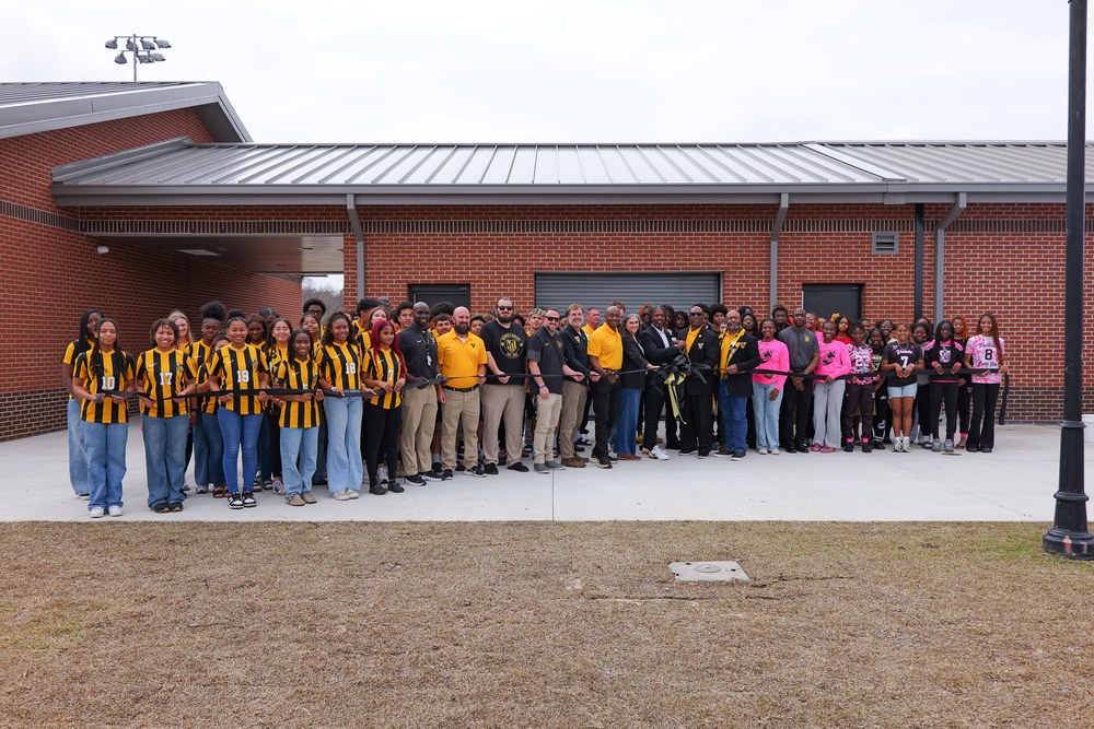 group photo with staff and students holding the ribbon for the ceremony