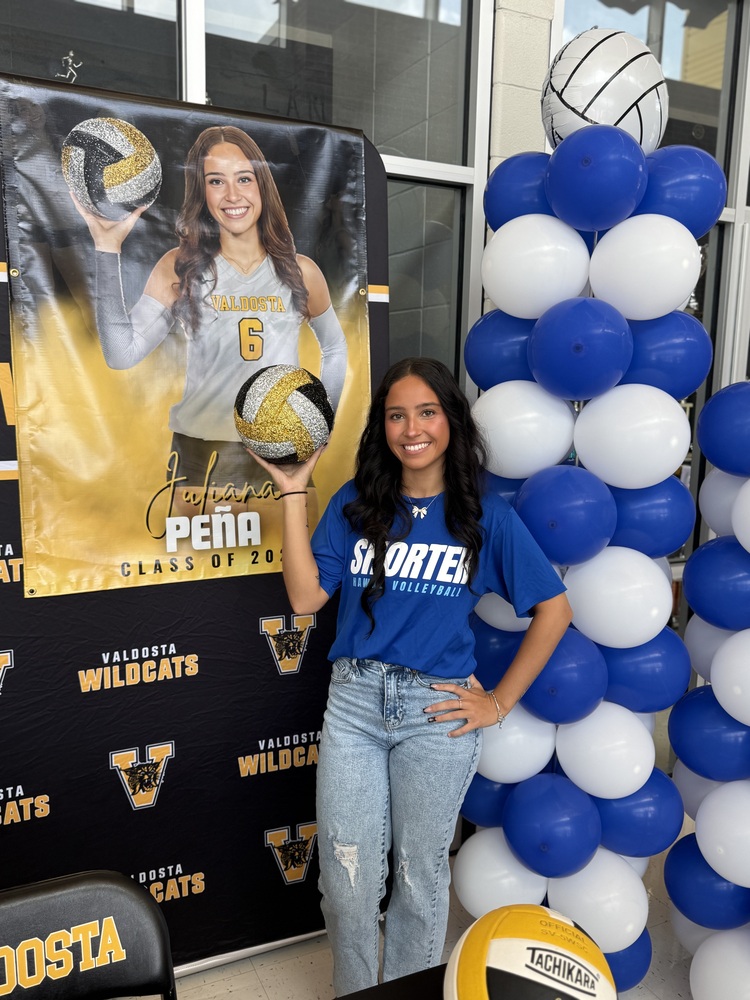 Juliana holding sparkly black, gold, and silver volleyball in front of her poster and blue and white balloon column