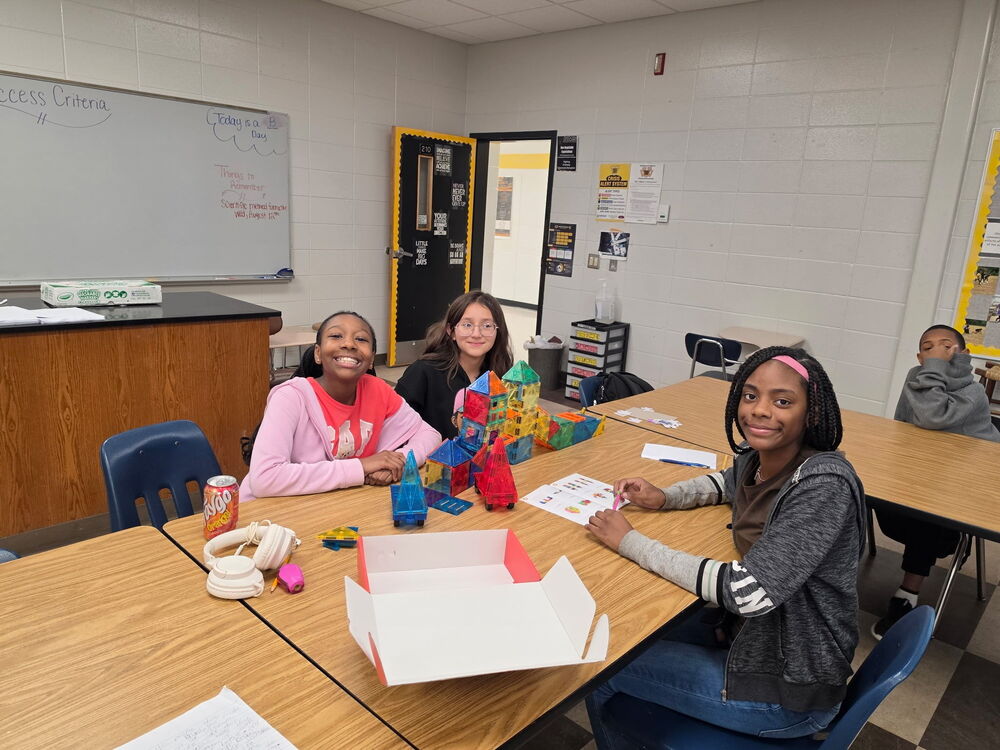 three students smiling at the camera while working on a project