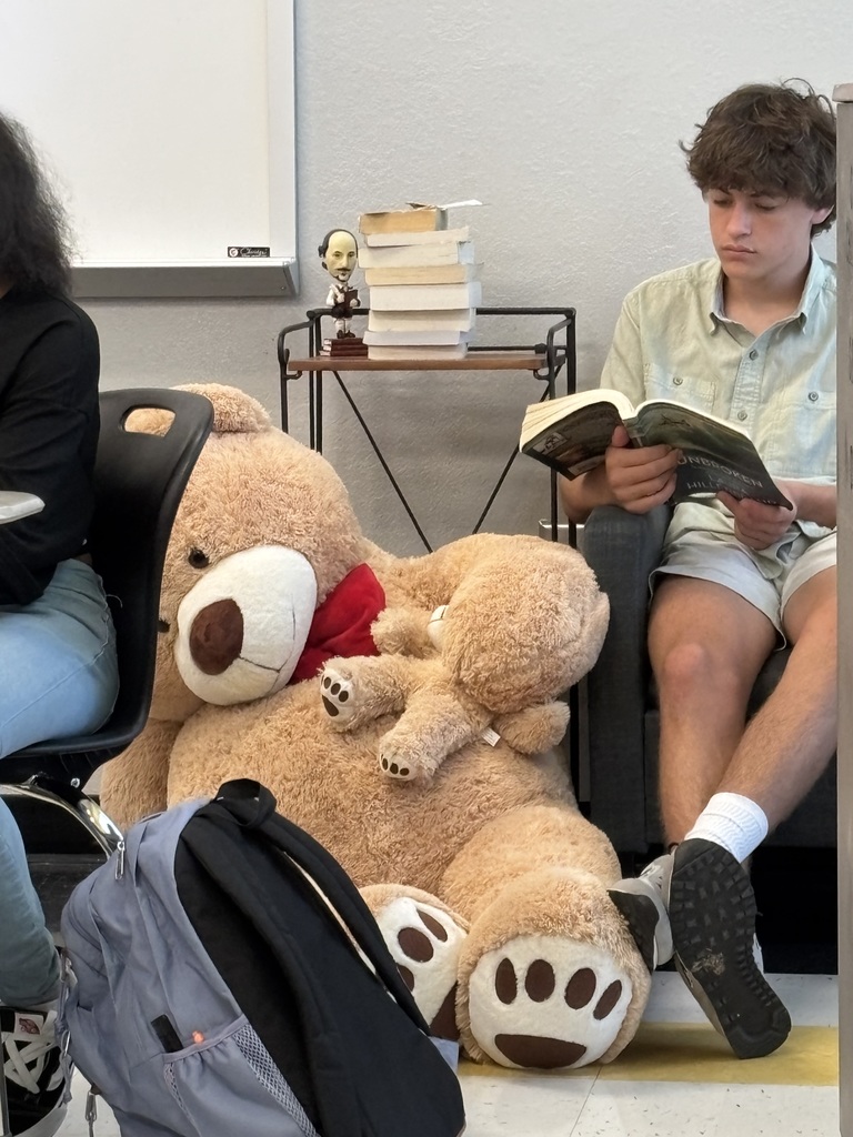 Lane reading in a chair next to a hugh teddy bear