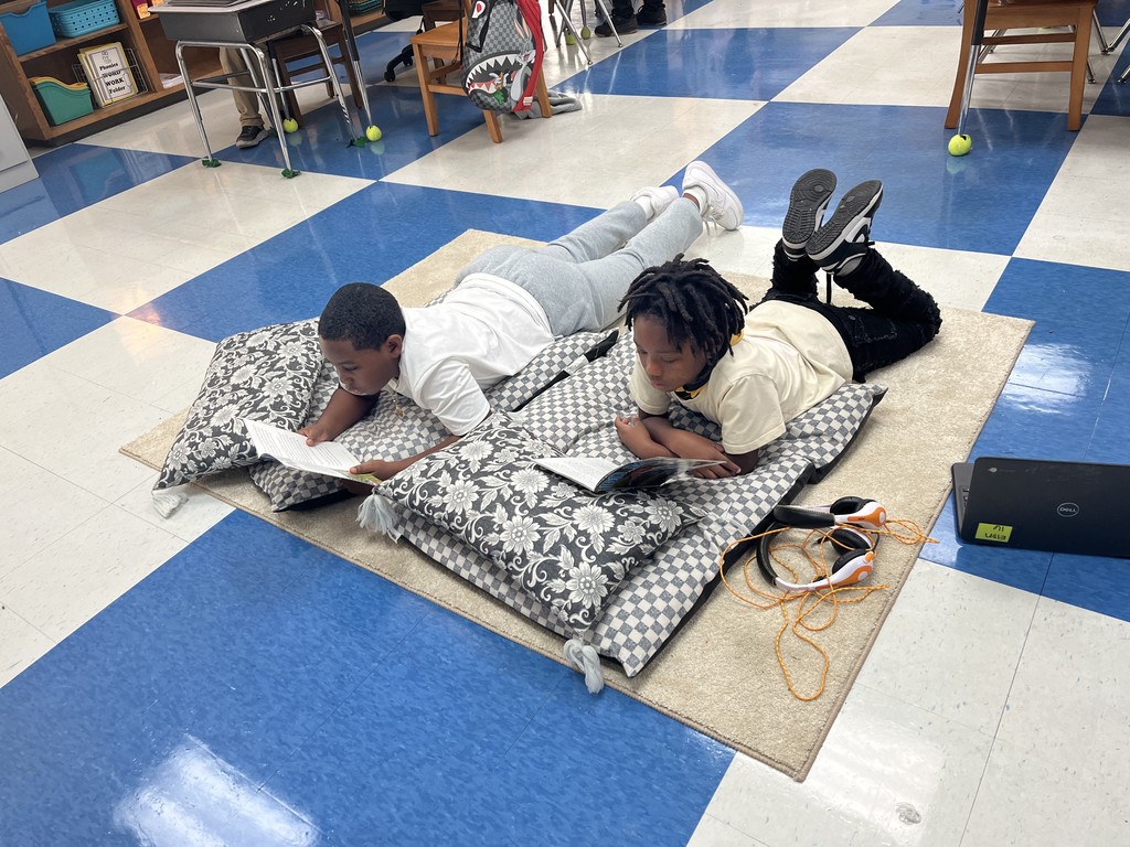 two students laying on the floor reading books on an area rug